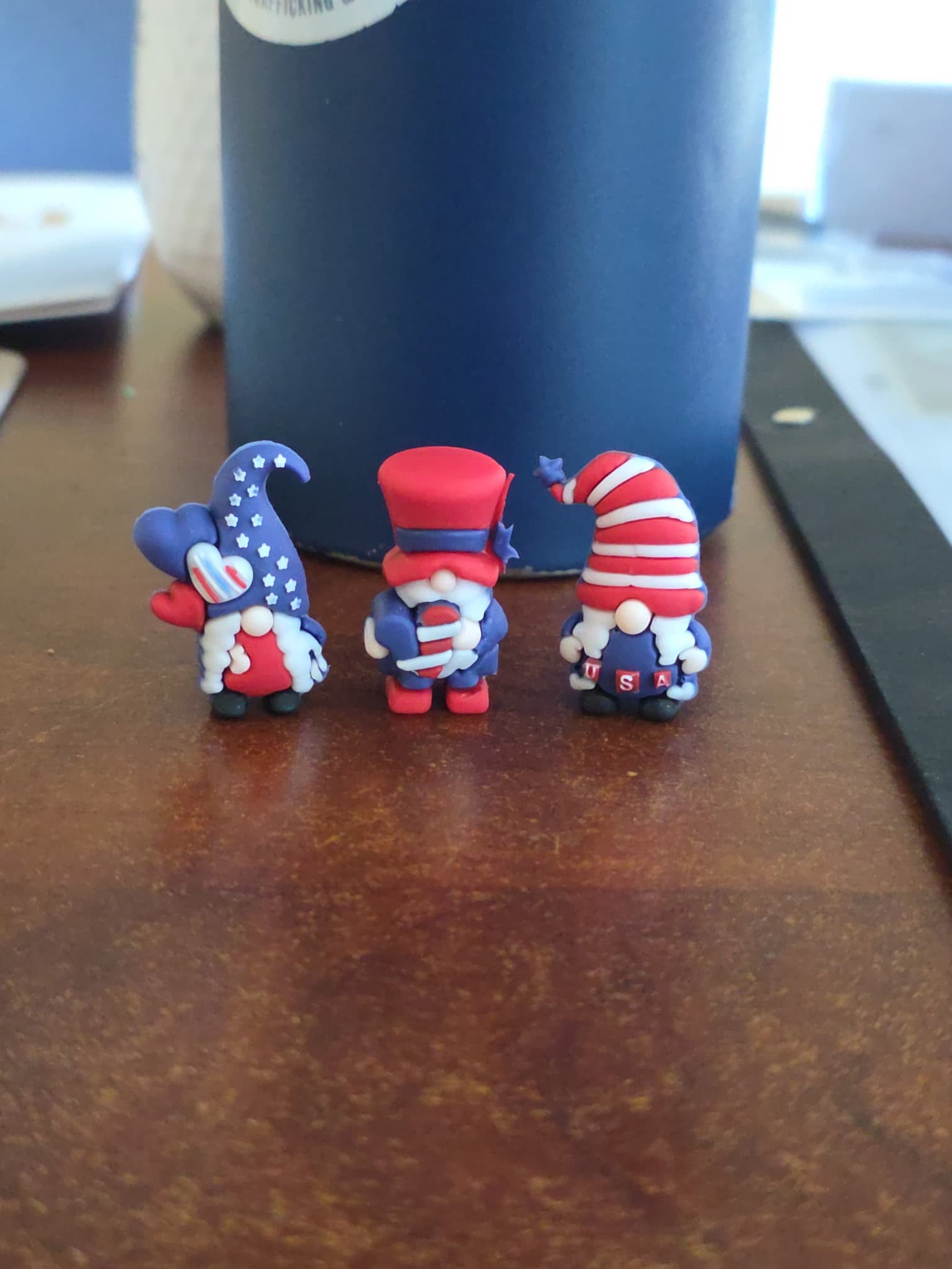 Three small handmade patriot gnomes left on a wooden desk beside a coffee mug